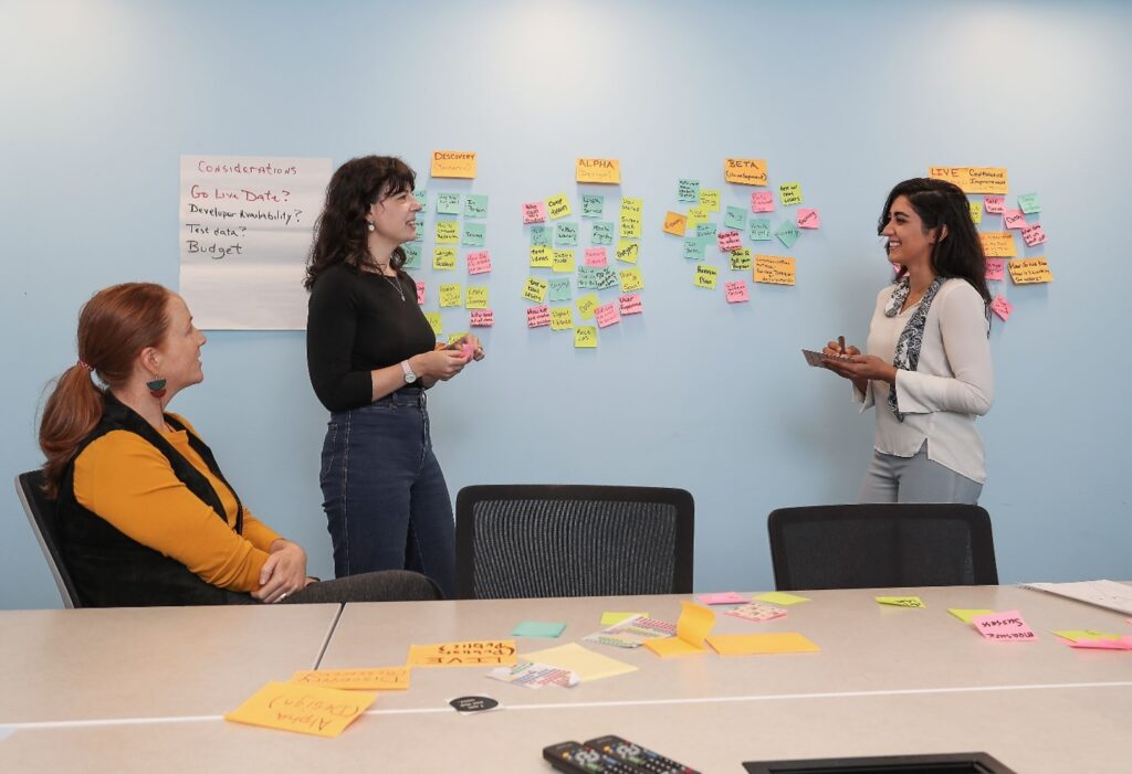 Three women using sticky notes on a wall to go work through a design task.