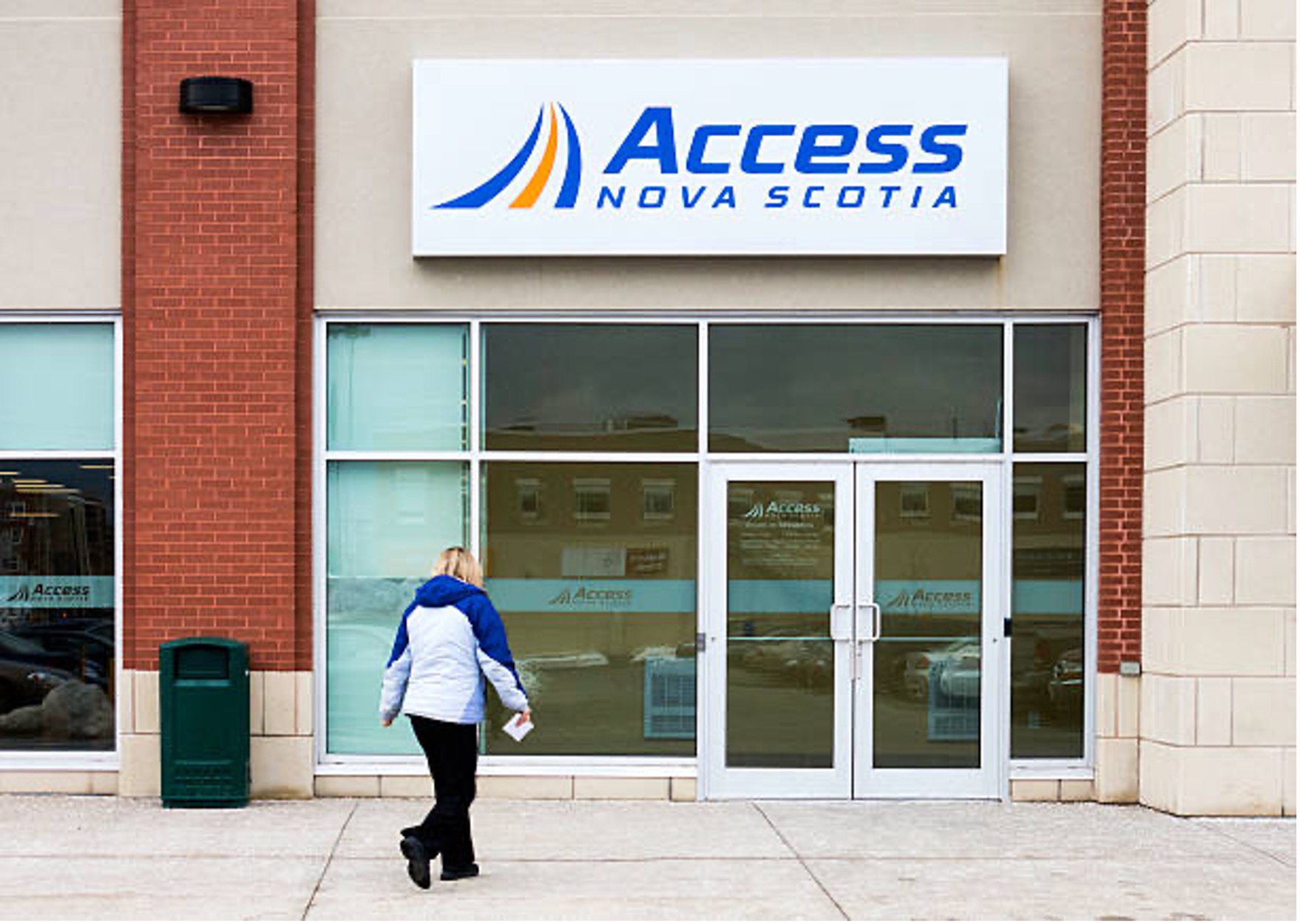 A person outside an Access Nova Scotia centre while holding a paper in their hand. They are approaching the front doors.