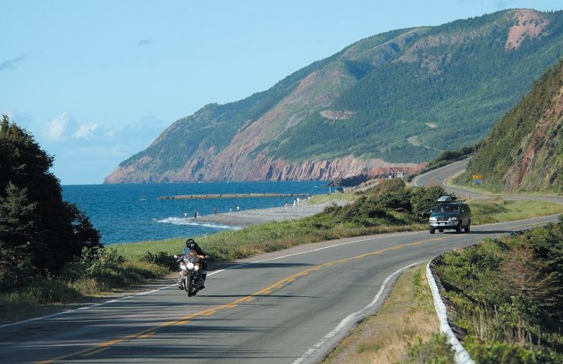 A motorcycle driving in front of a car on a winding road.