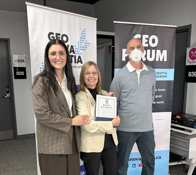 This picture shows Minister Jill Balser standing in front of two GEO Nova Scotia Banners with Bonnie Ste-Croix and Matt Spurway from GEO Nova Scotia. Bonnie is holding the Proclamation of Digital Inclusion Week.